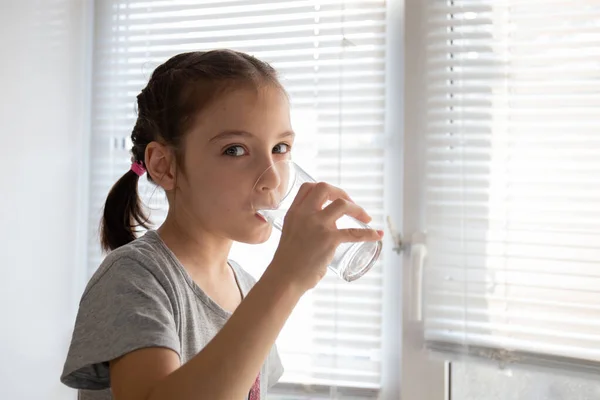 Gadis minum air dari gelas di pagi hari di rumah Stok Gambar