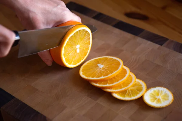 Pisau koki di tangan memotong jeruk menjadi irisan di papan potong Stok Gambar Bebas Royalti
