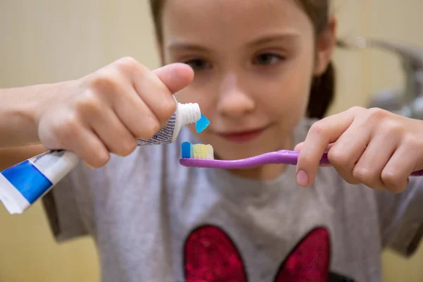 A little girl squeezes out toothpaste on to the brush. The concept of childrens health, medicine, prevention. — Stock Photo, Image