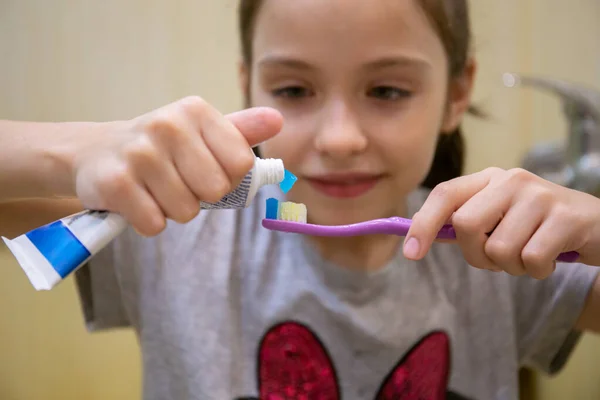 Seorang gadis kecil meremas pasta gigi ke sikat. Konsep kesehatan anak, obat-obatan, pencegahan. Stok Foto