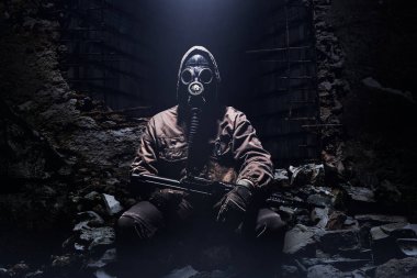 Tüfekli ve Sovyet koruyucu gaz maskeli bir takipçi savaşçının fotoğrafı. Arka plandaki harabelerde oturuyor..