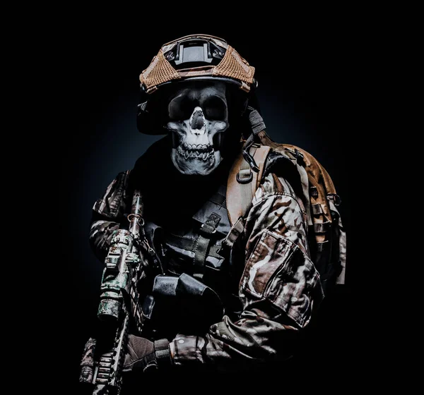 Photo of a fully equipped skeleton zombie soldier standing in armored vest and holding rifle on black background.