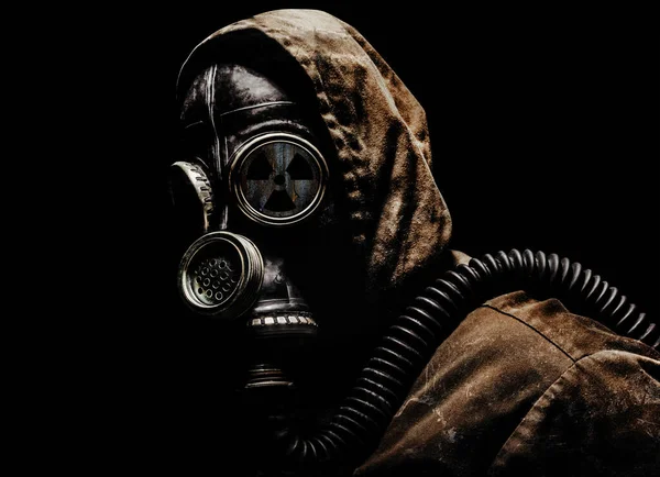 Stalker warrior in protective soviet gas mask standing on dark background with radiation sign.