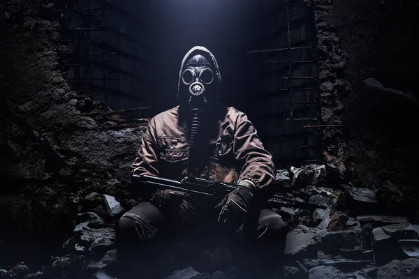 暗い背景に遺跡に座ってライフルとソ連の保護ゴム製のガスマスクを持つストーカー戦士の写真 — ストック写真