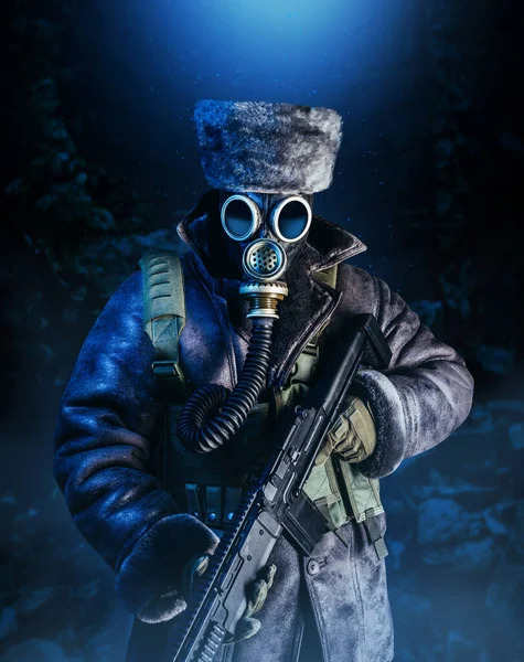 Photo of winter stalker soldier in fur coat, hat standing with pouch vest, gas soviet mask and rifle in stormy snowfall weather, full torso view.