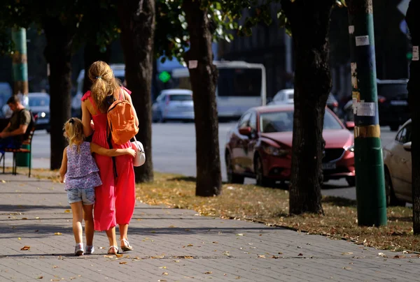 娘は母親を抱きしめる。お母さんと一緒に通りを歩いてる女の子 — ストック写真