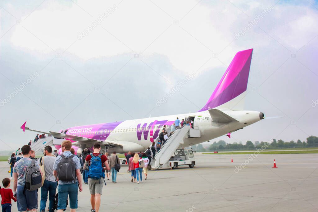 The image shows a group of passengers walking on the tarmac towards an aircraft that has a distinctive purple tail fin. The aircraft appears to be a commercial passenger jet, and the livery indicates
