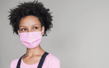 Koruyucu yüz maskesi takan sevimli küçük bir kız. Gri arka planda izole edilmiş maskeli çocuk portresi. Salgın, salgın, korona virüsü koruması, sağlıklı yaşam tarzı, peol konsepti