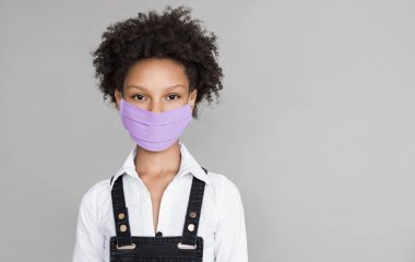 Koruyucu yüz maskesi takan sevimli küçük bir kız. Gri arka planda izole edilmiş maskeli çocuk portresi. Salgın, salgın, korona virüsü koruması, sağlıklı yaşam tarzı, peol konsepti