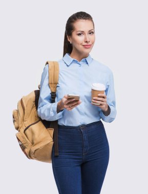 Akıllı telefonu ve gri arka planda izole edilmiş bir fincan kahvesi olan genç ve güzel bir kadın, şirin bir öğrenci portresi. 