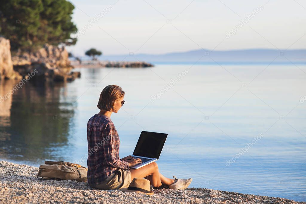 Young woman using laptop computer on a beach at sunset, travel and freelance work concept