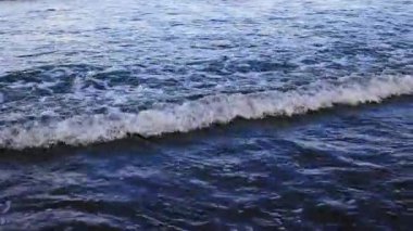 Dinamik okyanus dalgaları çarpışıyor ve sakin bir kıyı şeridinde geri çekiliyor.