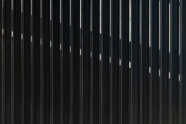 Işık çizgilerini yansıtan dikey parmaklıkları olan parlak siyah metal çitler..