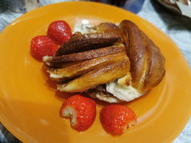 Yumuşak, tatlı tarçınlı çörek ve yuvarlak tabakta çilek.