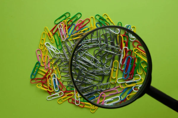 a palette of different paper clips are on the table, magnifying the paper clips with a magnifying glass