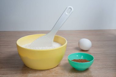 Mutfak masasının üzerinde bir kase un ve kakao duruyor, arka planda bir yumurta.