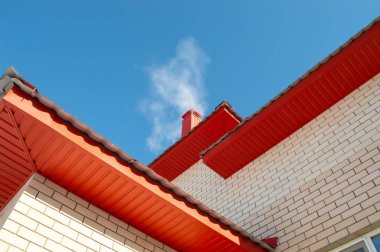 Yakın plan - kırmızı çatıdaki bacadan gelen duman soğuk bir günde, mavi gökyüzüne karşı