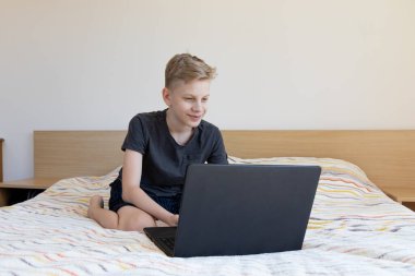 Çocuk çalışmak için aletler kullanıyor. Evde ödev yapıyorum. Laptop yatağın üstünde. Karantina sırasında evde eğitim.