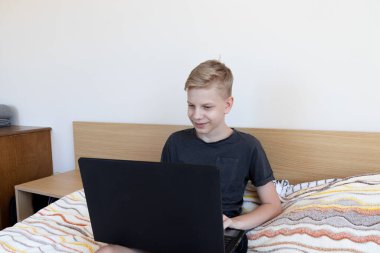 Çocuk çalışmak için aletler kullanıyor. Evde ödev yapıyorum. Laptop yatağın üstünde. Karantina sırasında evde eğitim.