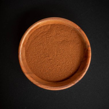 Kara arka planda izole edilmiş ahşap bir kasede yer tarçın. Üst manzara, düz uzanma.