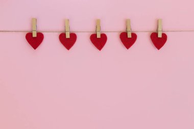 Red hearts hanging on the clothesline on pink background. Love, Wedding, Romantic and Happy Valentine day holiday concept. clipart