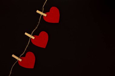 Kırmızı kalp çamaşır ipinde asılı. Tebrik kartı için el yapımı, siyah arkaplanda izole edilmiş. Sevgililer Günü