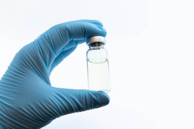 Mavi eldivenli Doktor Eli şişeyi aşıyla ya da beyaz arka planda uyuşturucuyla tutuyor. Coronavirus aşısı çalışma konsepti.