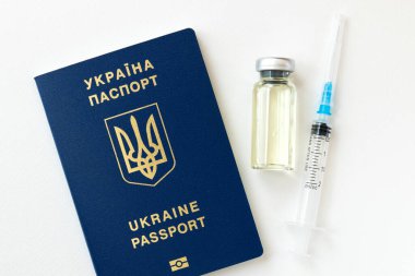 Coronavirus aşısı şişesinin ve beyaz arka planda Ukrayna mavi pasaportlu bir şırınganın yakın plan görüntüsü..
