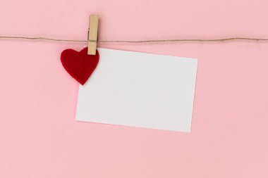 Pembe arka planda çamaşır iğnesiyle ipe tutturulmuş beyaz bir kağıt parçası. Sevgililer Günün kutlu olsun..