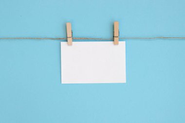 Notlar için boş kağıt çarşaf, çamaşır mandallı bir ipe asılan çerçeveler ve mavi arka planda izole edilmiş. Metin için boş alanı olan beyaz boşluk.