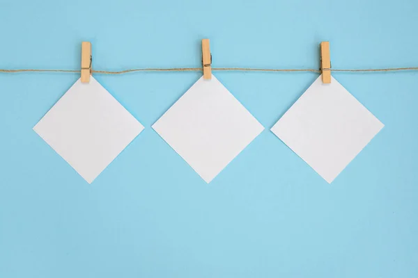 Empty paper sheet for notes, frames that hang on a rope with clothespin and isolated on blue background. White blank with empty space for text.