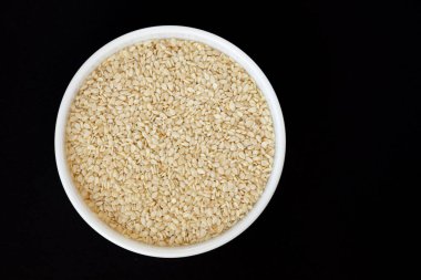 Siyah zemin üzerinde izole edilmiş beyaz seramik kasedeki susam tohumları, üst görünüm, yakın çekim