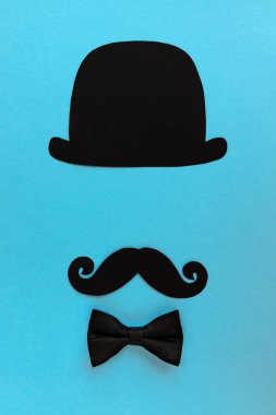 Mutlu Babalar Günü kartı, siyah şapkalı kompozisyon, bıyıklı ve papyonlu. Mavi arka planda izole edilmiş metin için boş alan var.