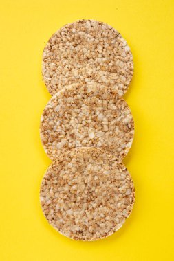 Sarı arka planda çıtır çıtır pirinç kekleri, izole edilmiş üç tane tam tahıllı çıtır ekmek, kapat.