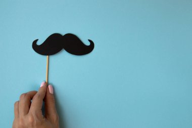 Creative Square Flatlay, mutlu Babalar Günü, geçmişe dönük siyah fotoğraf kabini, kadın elinde bıyık, mavi arka planda boş alan, erkekler sağlık farkındalığı, ay babaları günü, erkeklik kavramı.