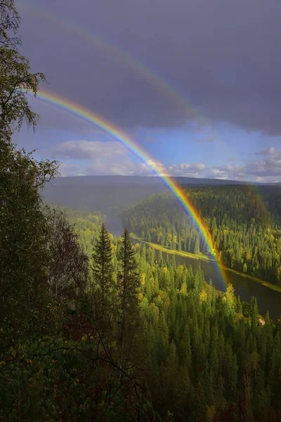 A multicolored rainbow over the autumn Ural forests and the Usva River near the Usvinskie Stolby stone (Gremyachinsky District, Perm Territory) at sunset.