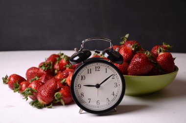 Tablo ve eski tarz kırmızı masa saati üstünde taze çilek