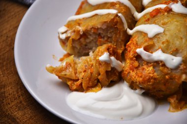 Lahana yaprakları lahana dolması etli plaka üzerinde bir peçete, domates, maydanoz ve sarımsak soluk ahşap tahta bir arka plan üzerine domates sosu