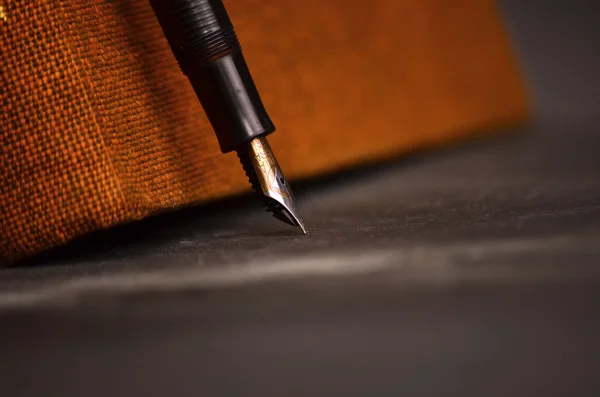 Caneta elegante deitado em um livro contra um fundo preto — Fotografia de Stock