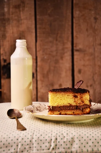 Morceau de gâteau avec la bouteille de lait sur la nappe — Photo