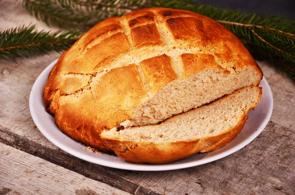 Fresh home baked bread is lying on  a wooden table with Christmas tree branch — Stock Photo, Image