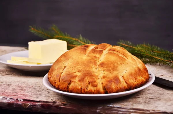 Pão caseiro fresco está deitado em um prato branco em uma mesa de madeira ao lado de um prato com o comprador. Natal. — Fotografia de Stock