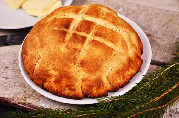 Pão caseiro fresco está deitado em um prato branco em uma mesa de madeira ao lado de um prato com o comprador. Natal. — Fotografia de Stock