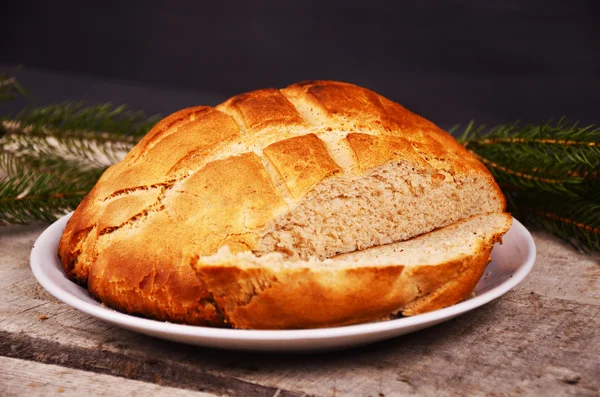 Fresh home baked bread is lying on  a wooden table with Christmas tree branch — Stock Photo, Image