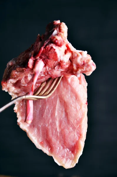 Fresh uncooked rib-eye steak with large fork on black background — Stock Photo, Image