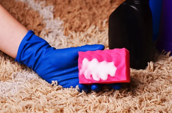 People, housework and housekeeping concept - close up of woman in rubber gloves with cloth and detergent spray cleaning carpet at home — Stock Photo, Image