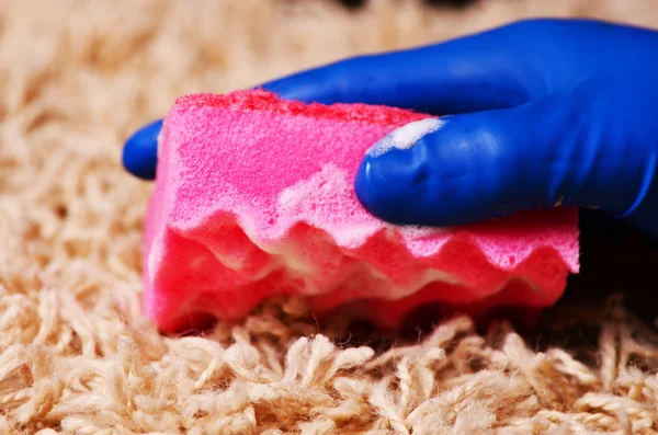 People, housework and housekeeping concept - close up of woman in rubber gloves with cloth and detergent spray cleaning carpet at home — Stock Photo, Image