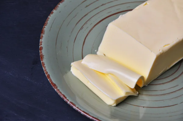 Pat of fresh farm butter on a butter dish with a knife to use as a spread or cooing ingredient, overhead view on a slatted wooden table — Stock Photo, Image