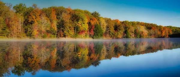 Rose Lake on foggy morning. Mist over water with colorful trees in hocking hills ohio on clear fall morning. Autumn tones of red, yellow, and orange in trees on waters edge. Reflection visible.