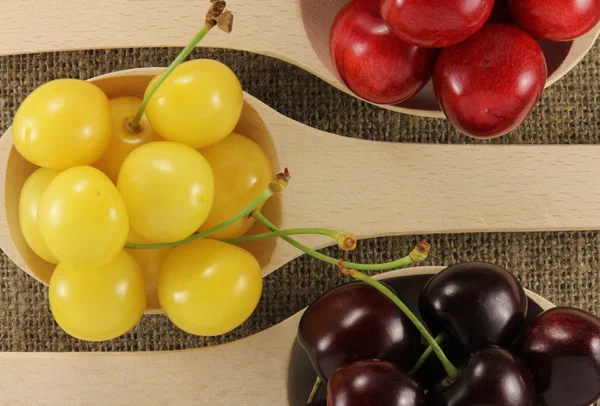 Colorful cherries in a wooden spoon on a natural fabric — Stock Photo, Image